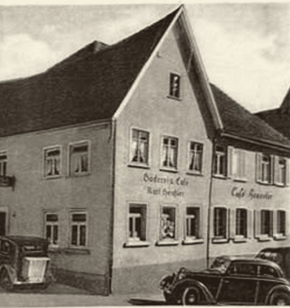 Giebelhaus mit der gemalten Aufschrift Bäckerei und Café Karl Heussler; davor parken Autos der 1930er Jahre.